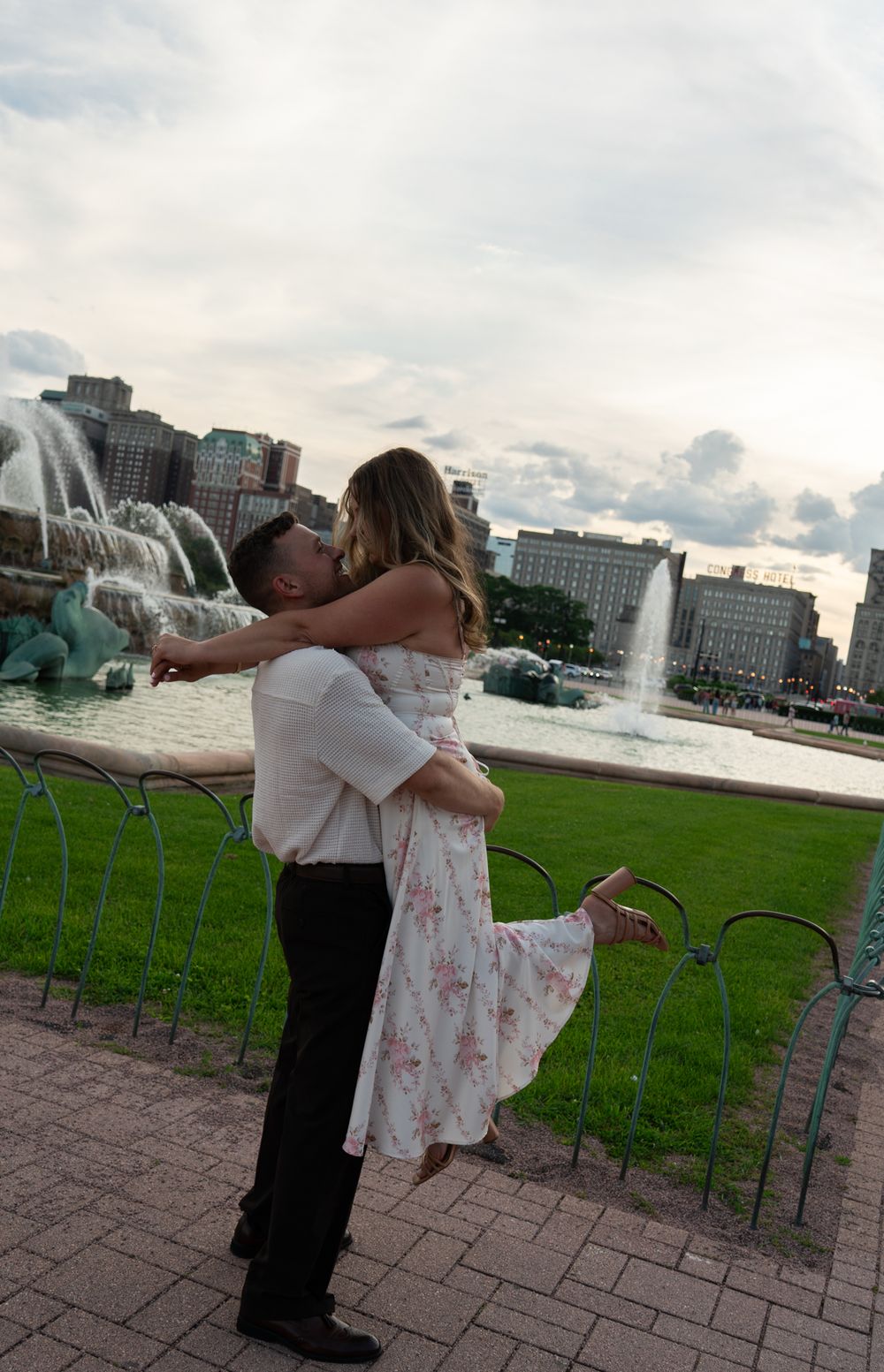 Man lifting woman in romantic embrace near Buckingham Fountain in Chicago at dusk.