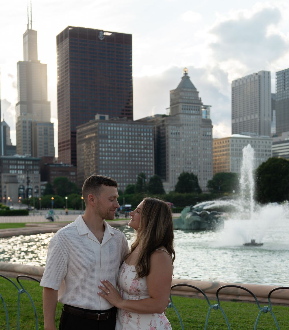 Couple embracing near Buckingham Fountain in Chicago with city skyline including Willis Tower in background.