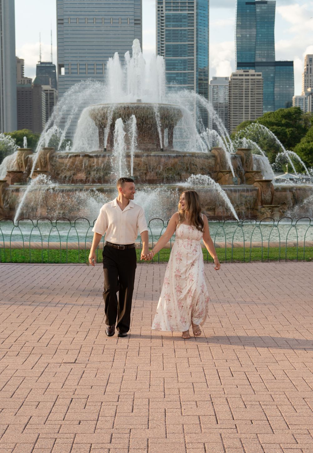 Couple holding hands walking in front of Buckingham Fountain with Chicago skyline backdrop.