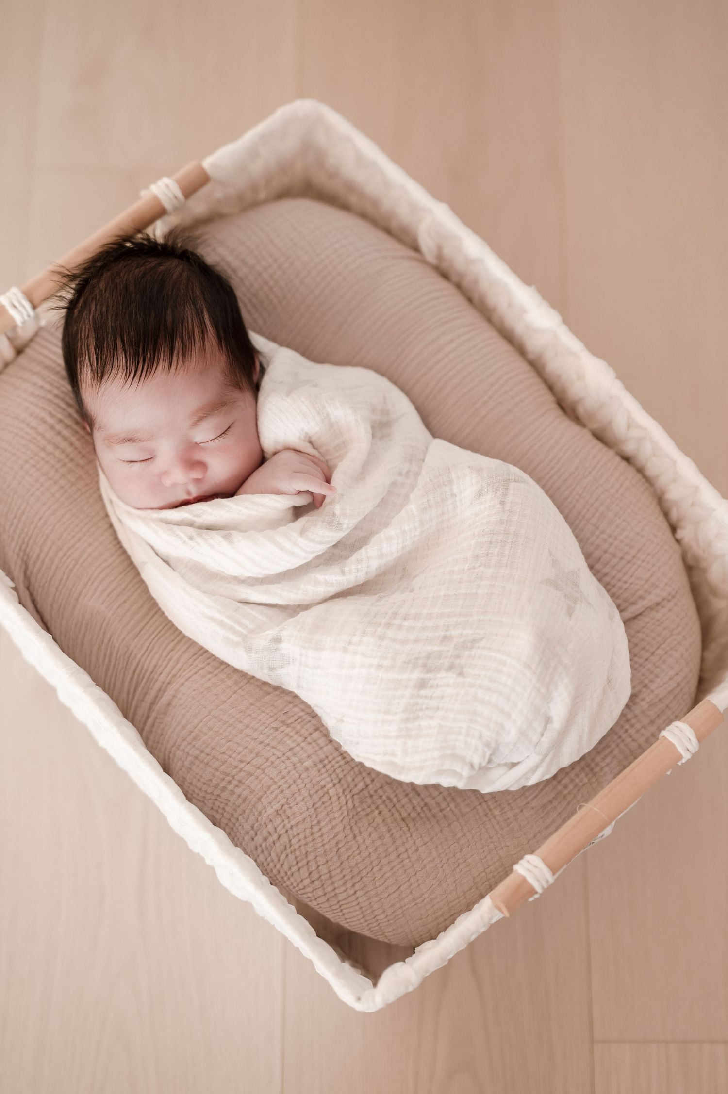 Sleeping newborn in white swaddle blanket rests peacefully on beige lounger pillow in progressive photo series.