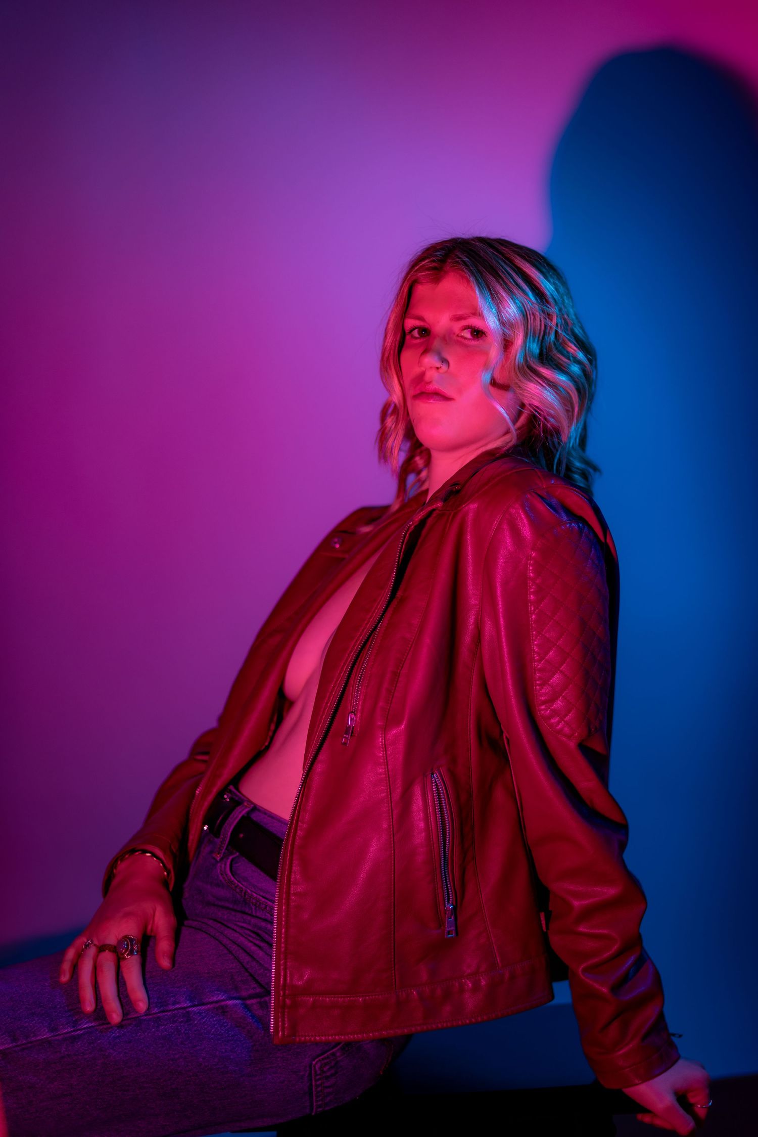A person in a red jacket poses dramatically against a neon-lit background with purple and blue lighting effects.