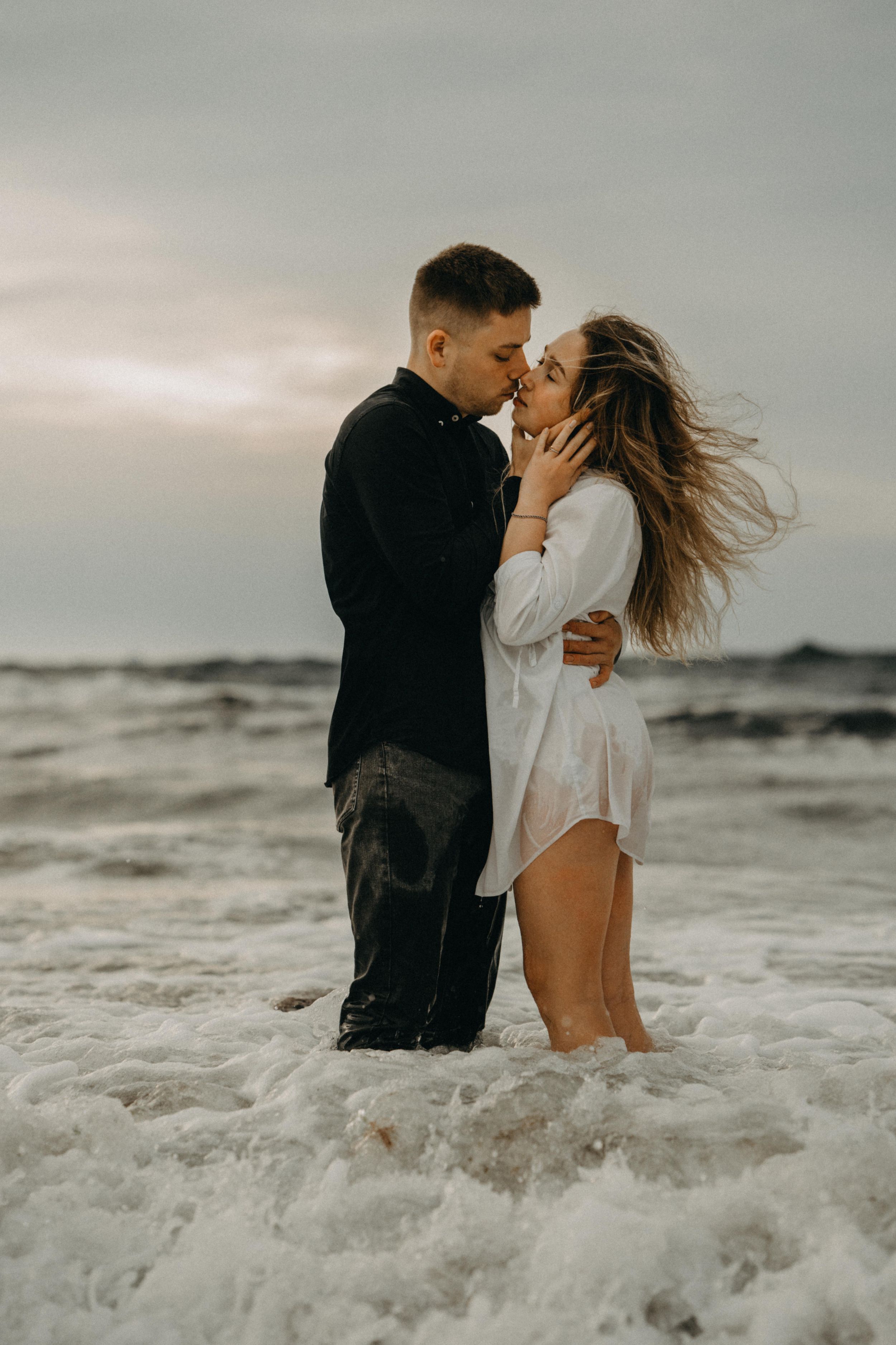 Romantic couple kissing in ocean waves at sunset on beach.
