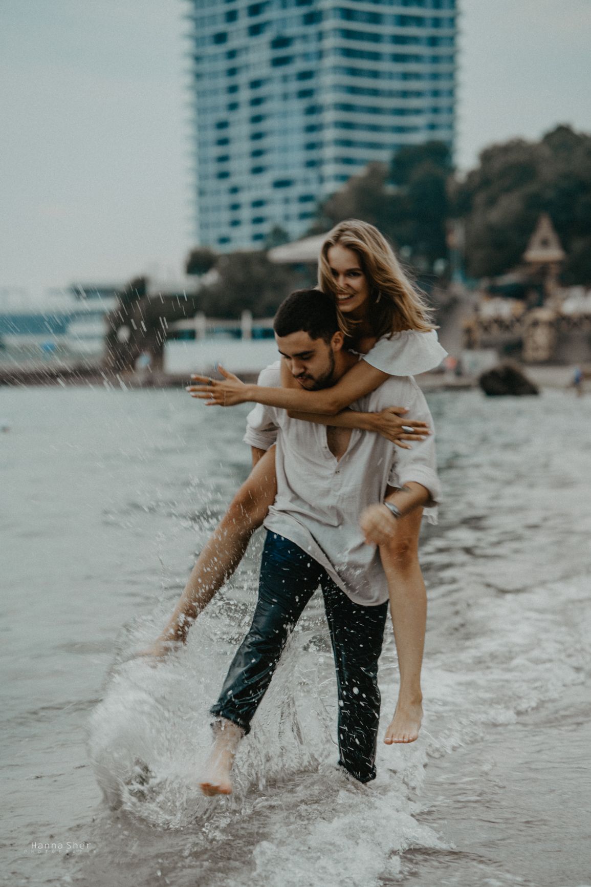 A joyful couple plays in ocean waves at the beach, with the man giving the smiling woman a piggyback ride.