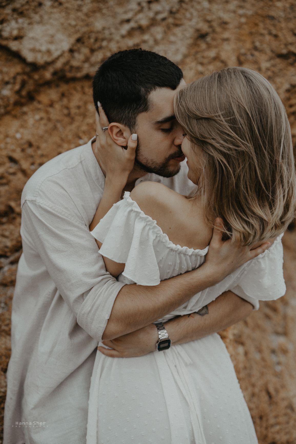 Couple sharing a kiss while embracing against a rocky background outdoors.