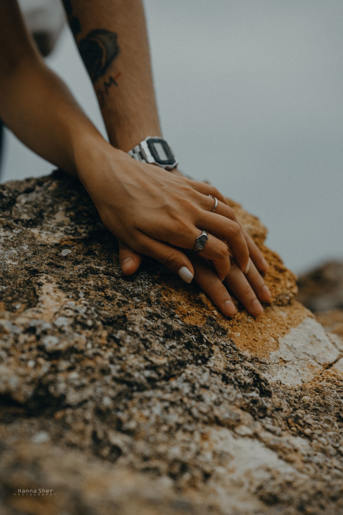 Two hands with rings resting together on a textured rock surface.