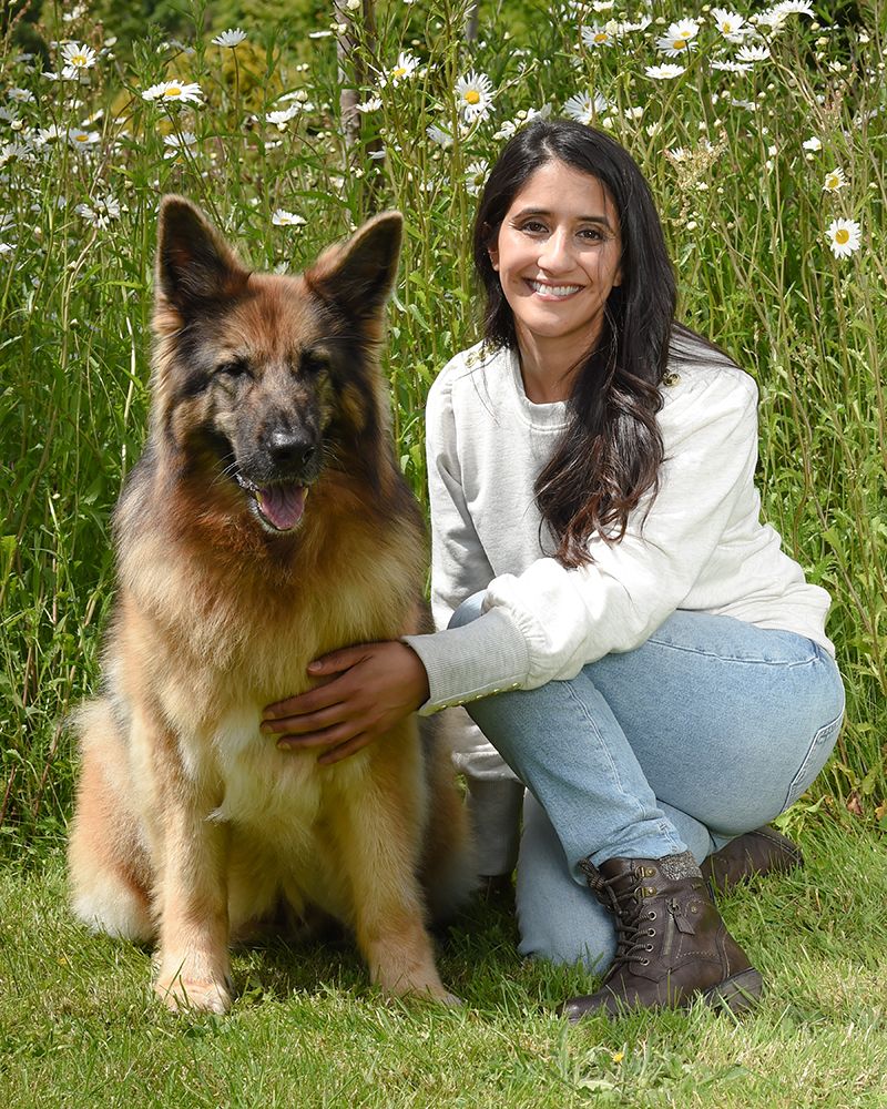 Fatima Maktari, founder of Tribal Pet Foods, sitting outdoors in wildflowers with her German Shepherd dog.