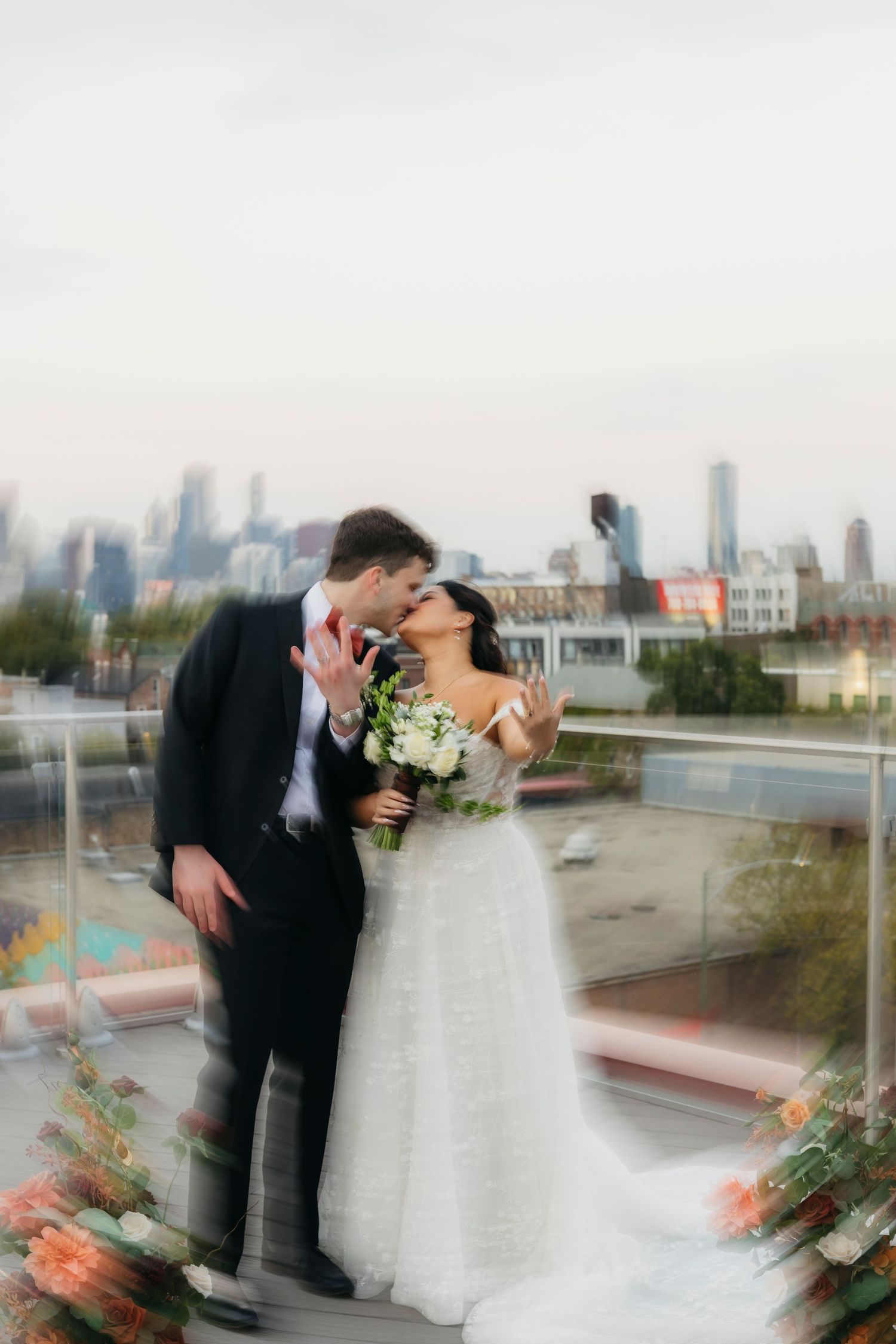 Romantic wedding couple embraces on a rooftop terrace overlooking Chicago skyline with floral arrangements.