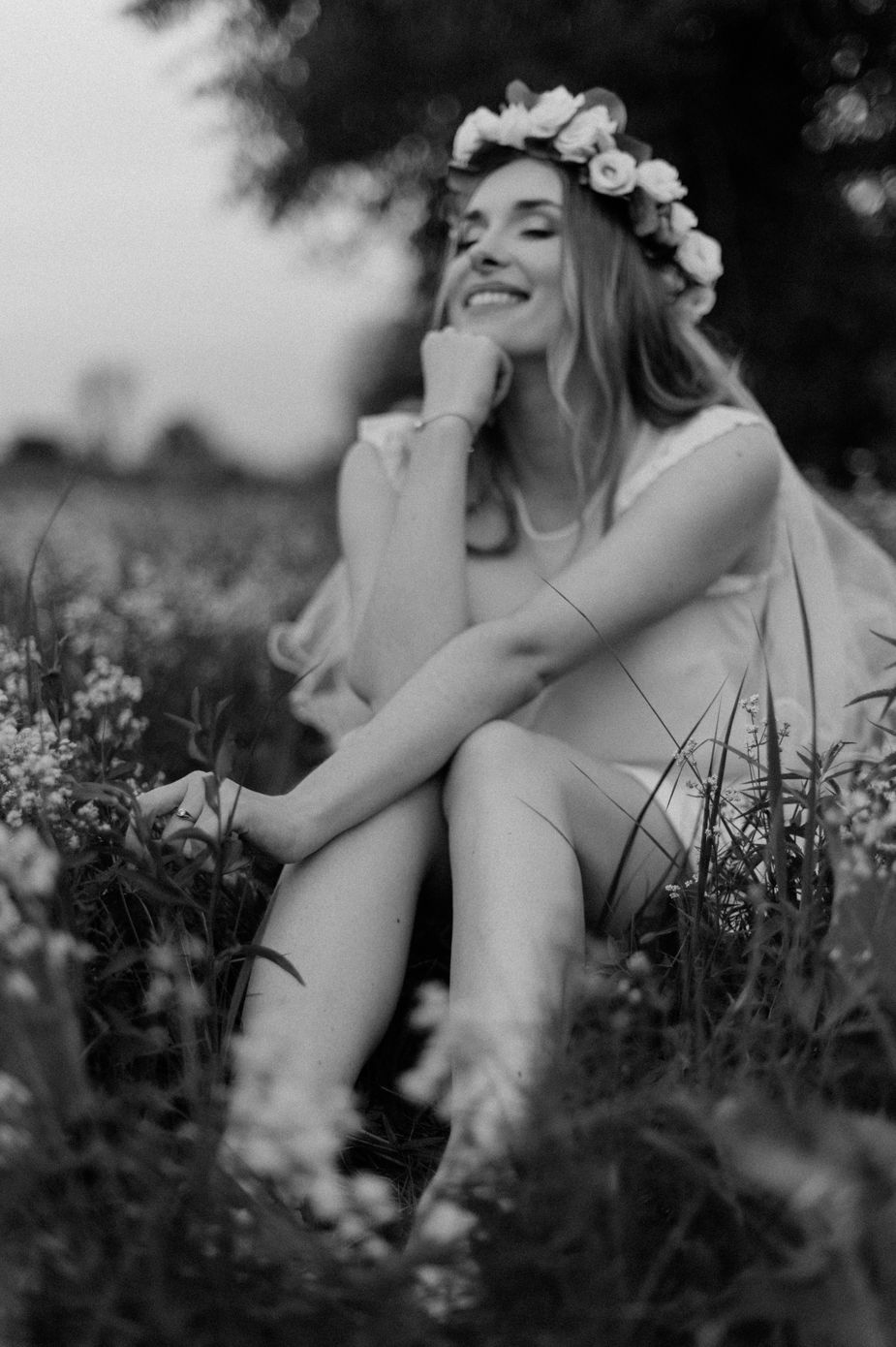 A dreamy black and white photo series shows a person in a floral crown relaxing in a wildflower meadow.