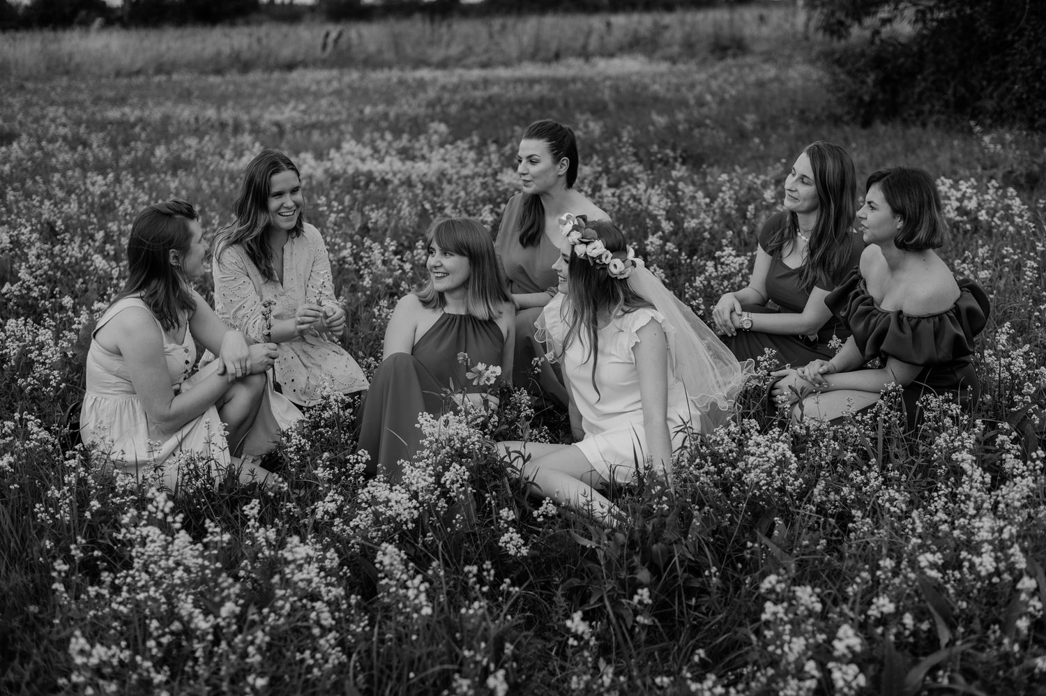Group of friends laughing and enjoying a sunny day together in a wildflower meadow, shown in black and white.