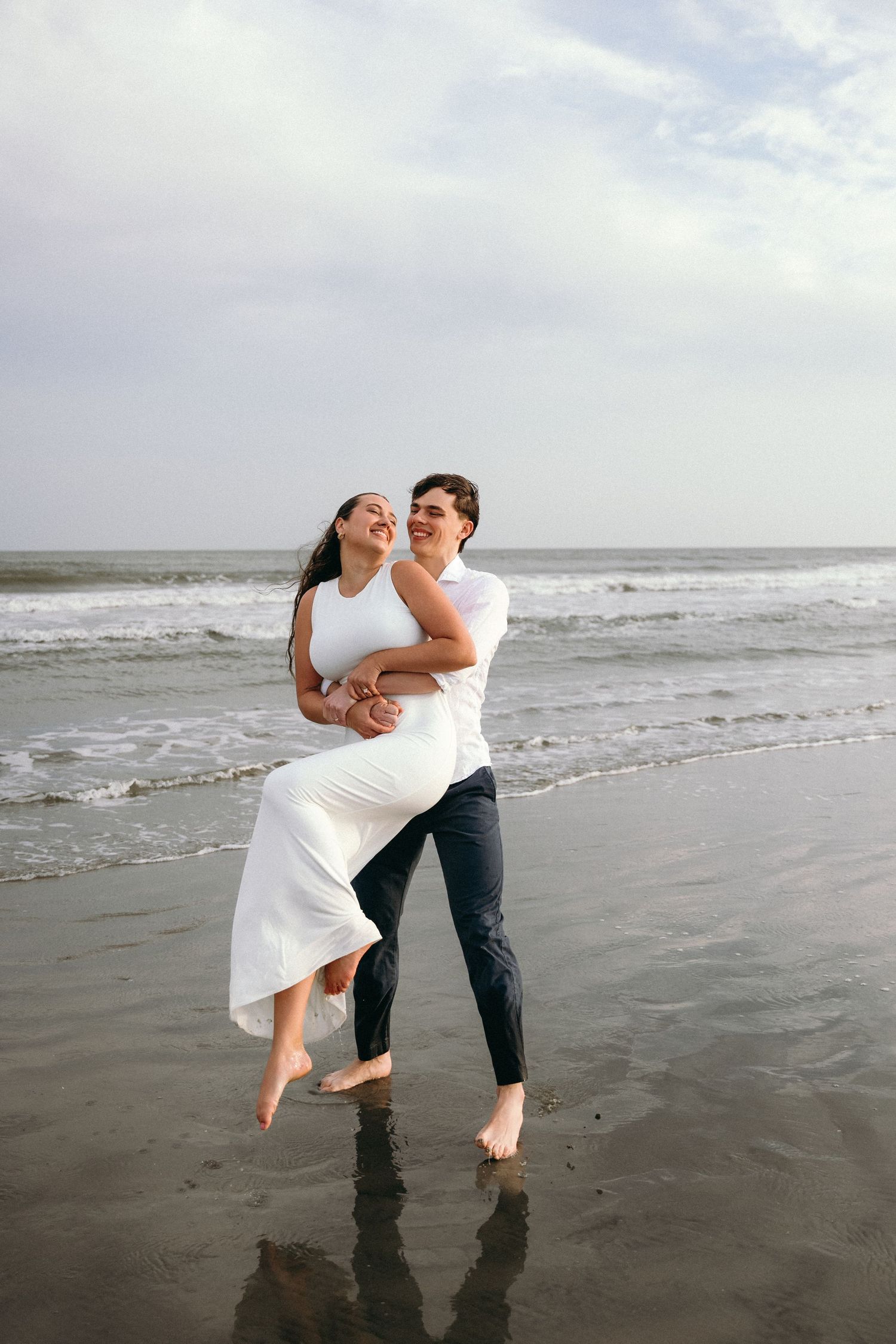 Romantic couple dancing and embracing on a moody beach with waves crashing in the background.