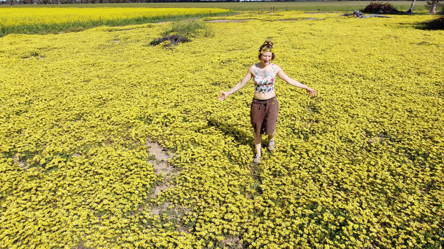 Sarah Thiessen, photographer for wild love media stands joyfully in a vast field of bright yellow wildflowers on a sunny spring day.