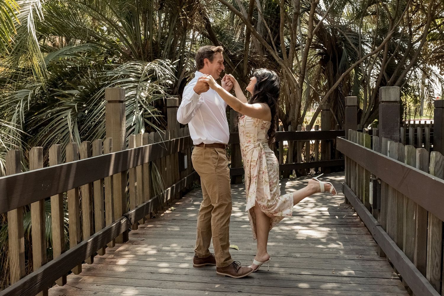 Couple dancing together along a shaded wooden boardwalk pathway surrounded by lush tropical palm trees at Balboa Park in San Diego.