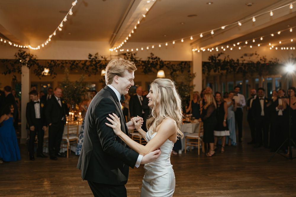A couple shares their first dance at a wedding reception under twinkling string lights in an elegant indoor venue.