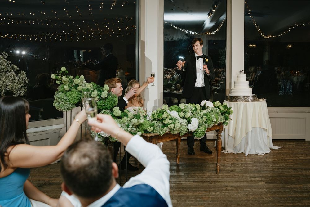 Wedding guests dance and celebrate on a dimly lit dance floor under string lights at an evening reception.