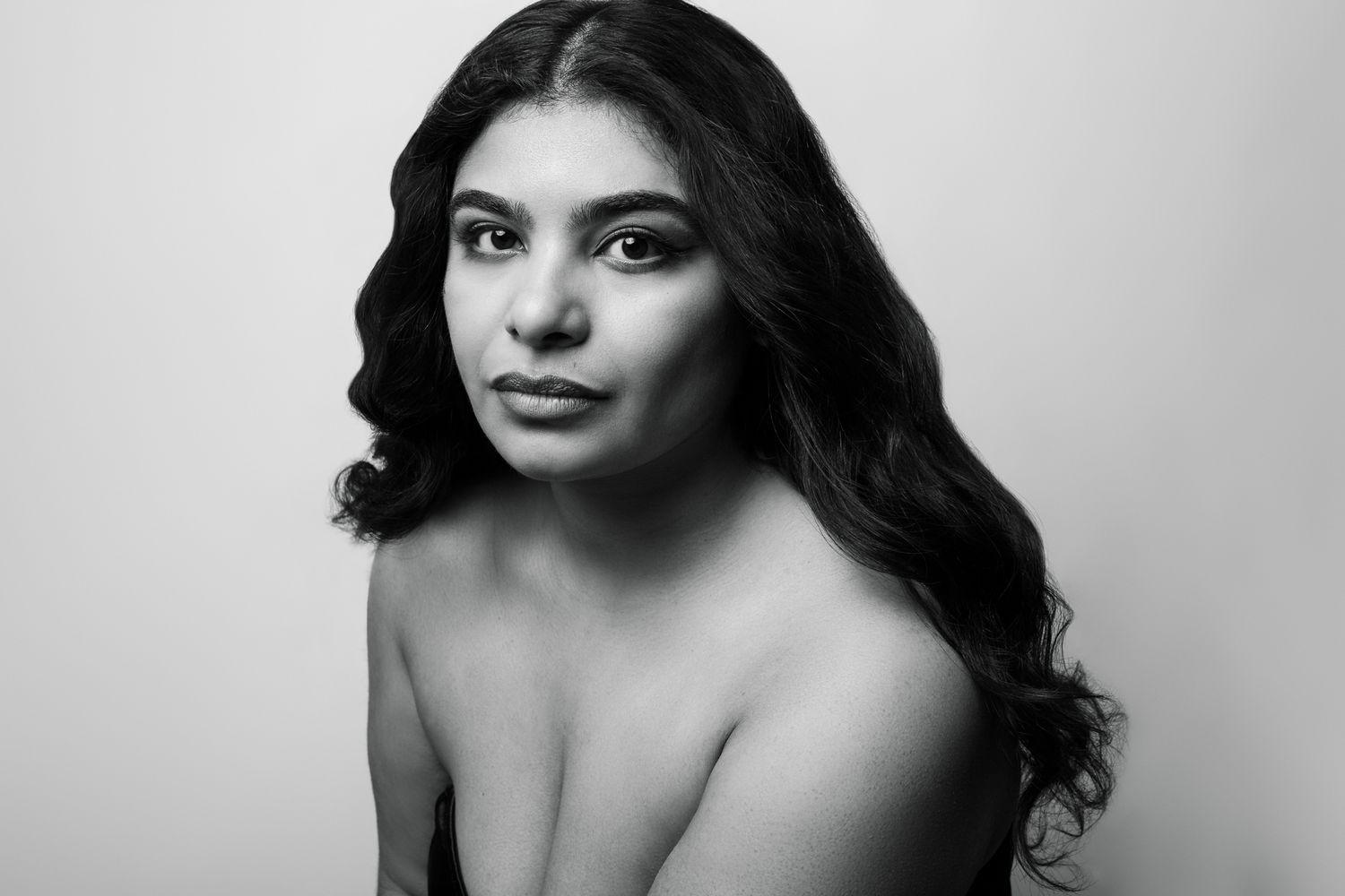Black and white portrait photograph showing shoulders and flowing dark hair against light background.