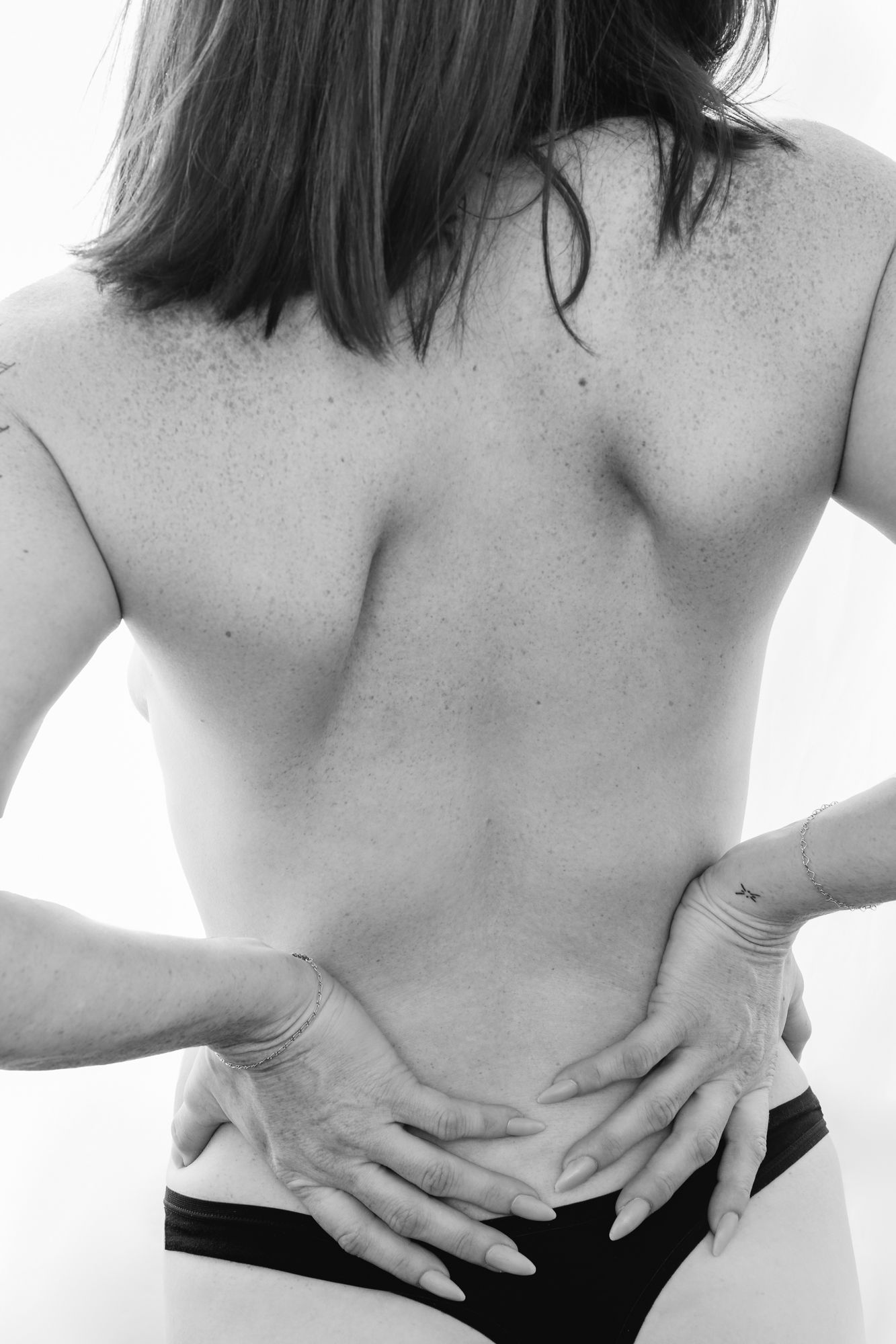 Black and white photograph of a bare back with hands placed on lower back showing body contours.