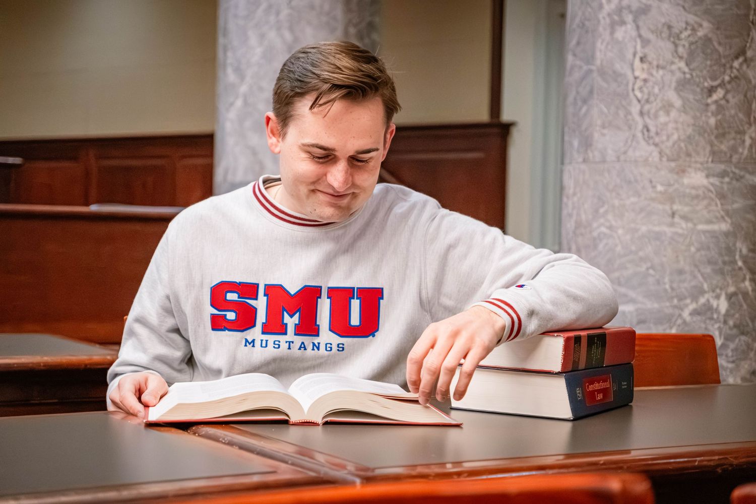 A student in an SMU sweatshirt studies with a textbook in a university building.