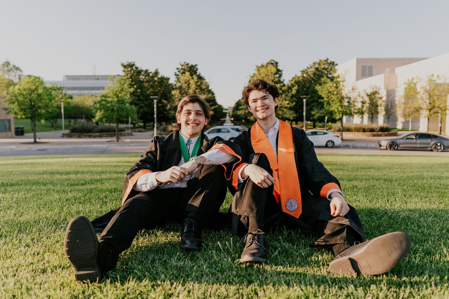 Graduates relaxing and celebrating on grass during sunset photo session.