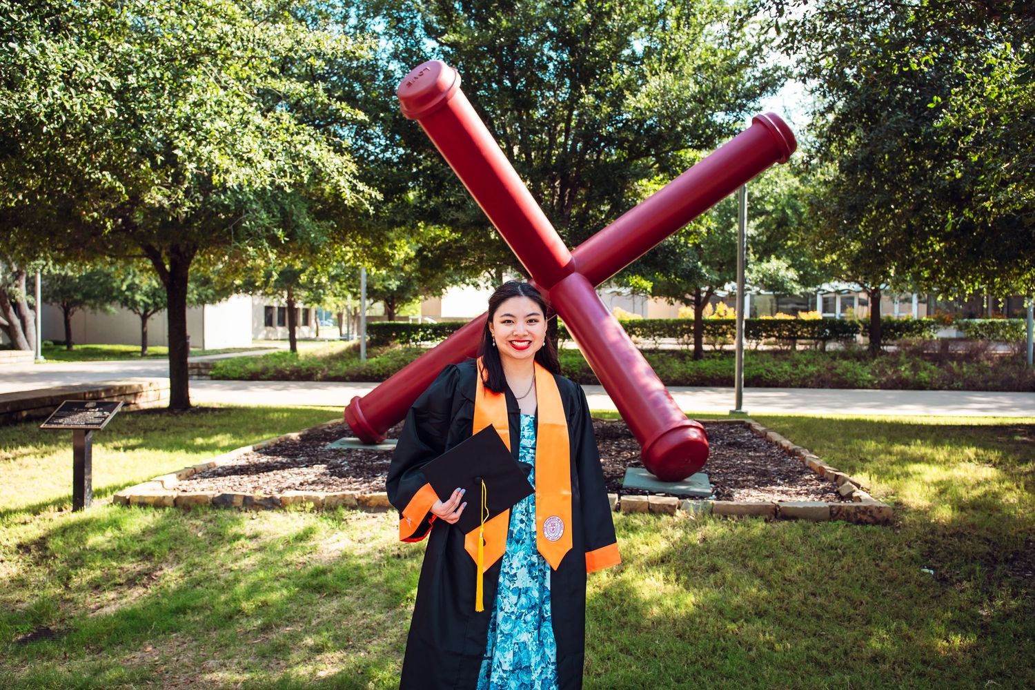 Graduate holding graduation cap with colorful decorations in outdoor campus setting. UTD Graduate Portraits by Eric Aaberg Phot