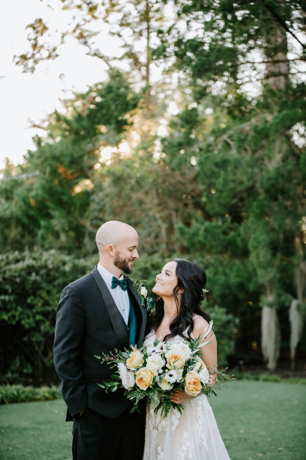 A couple shares romantic moments in an outdoor garden setting with elegant wedding attire and floral bouquet.