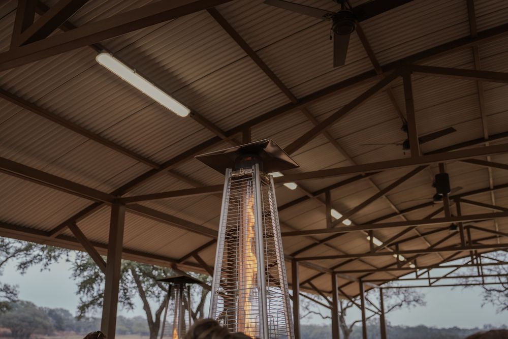 A modern outdoor patio heater with glowing flame tube illuminates a covered pavilion at dusk.