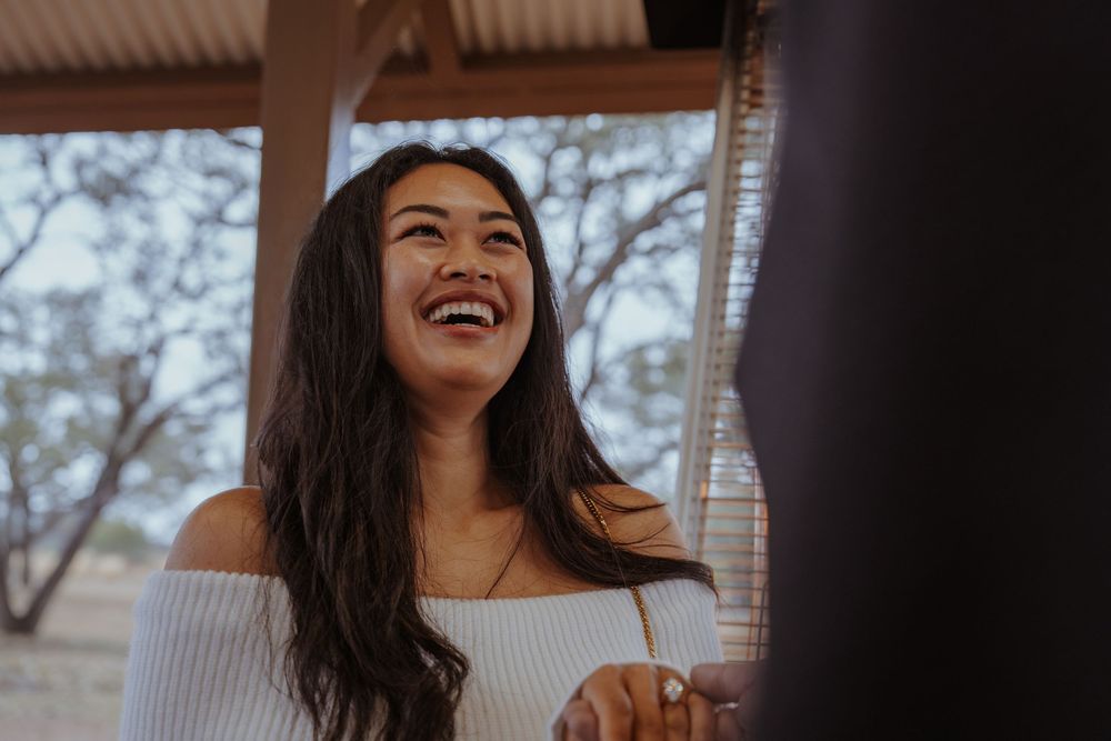 A woman in a white sweater laughs joyfully while sitting outdoors during a natural light photo session.