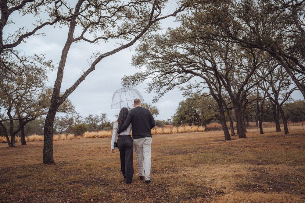 Panoramic landscape view of a couple walking among scattered trees in an autumn field at sunset.