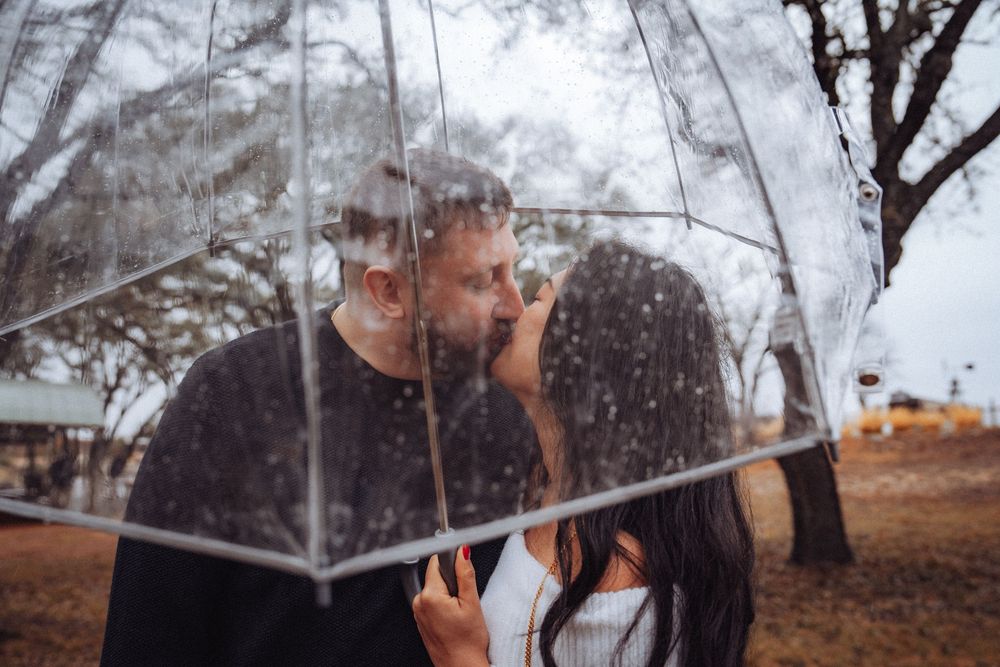 A couple shares an intimate moment under a clear umbrella in a misty autumn setting.