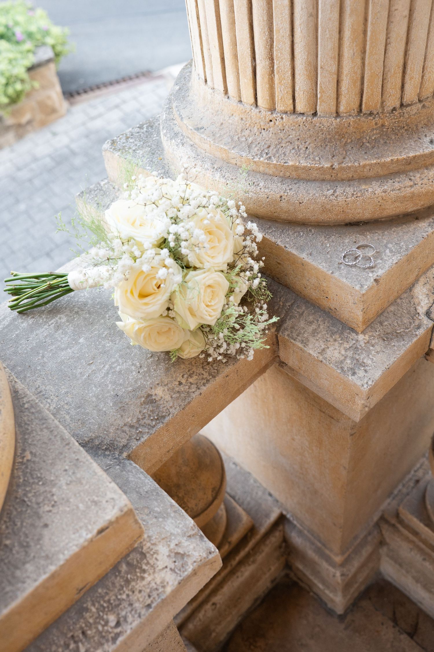 Delicate white roses and baby's breath bouquet rests on a stone ledge beside a fluted architectural column.