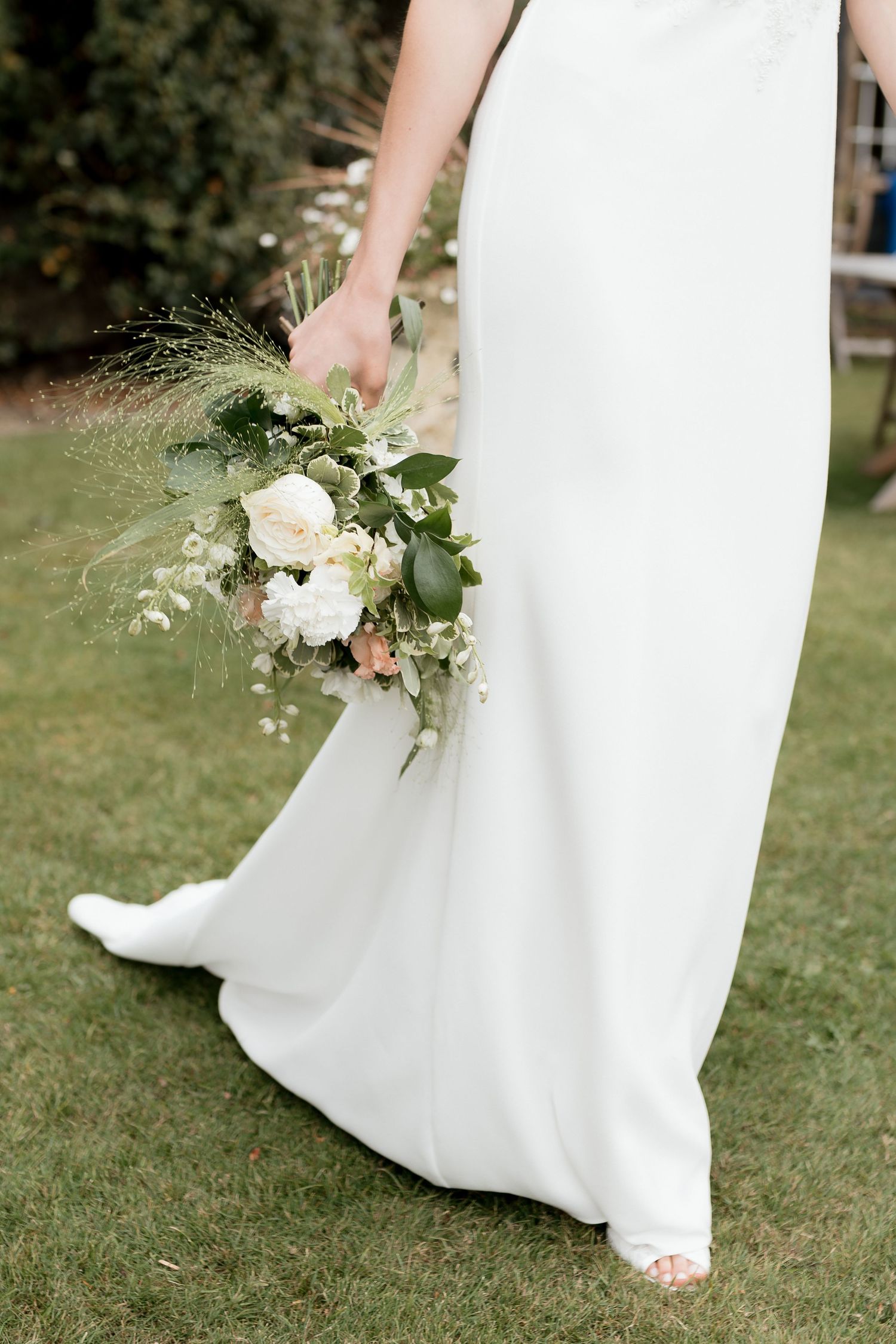 A blush pink wedding dress with ruffled tulle skirt hangs from a rustic wooden beam in a sunlit room.