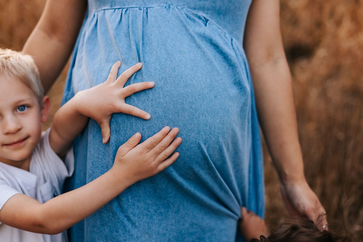 A person wearing a blue denim shirt holds a small child's hands in a tender moment outdoors.