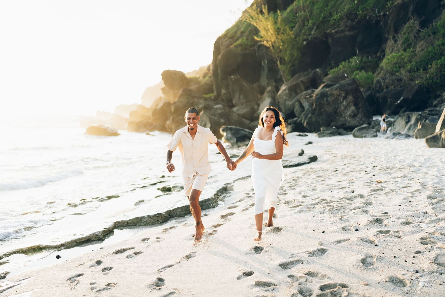Couple walking hand in hand along a scenic beach at sunset with waves crashing on the shore.