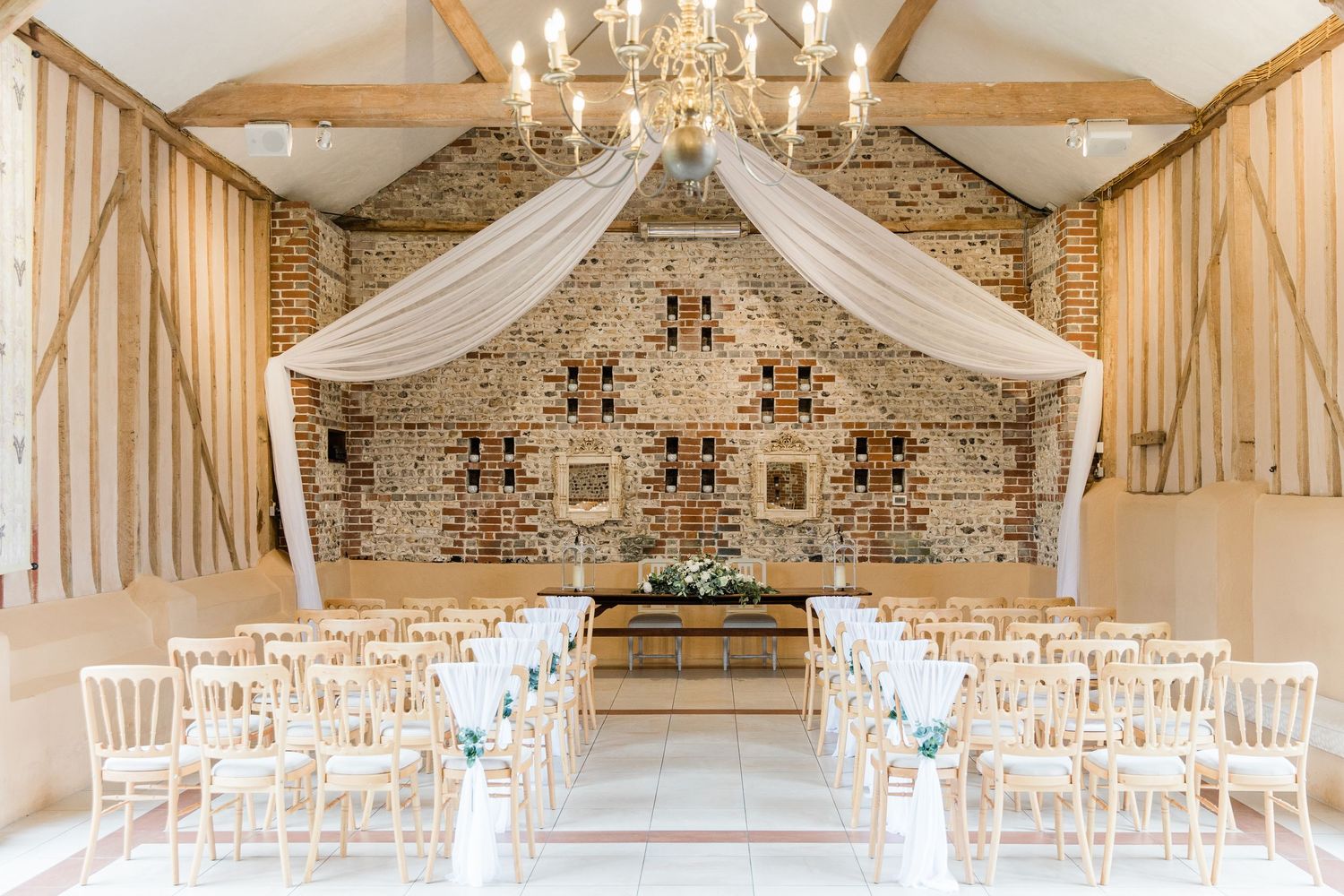 Elegant wedding venue with white drapes, chandeliers and exposed brick walls decorated for a romantic ceremony.