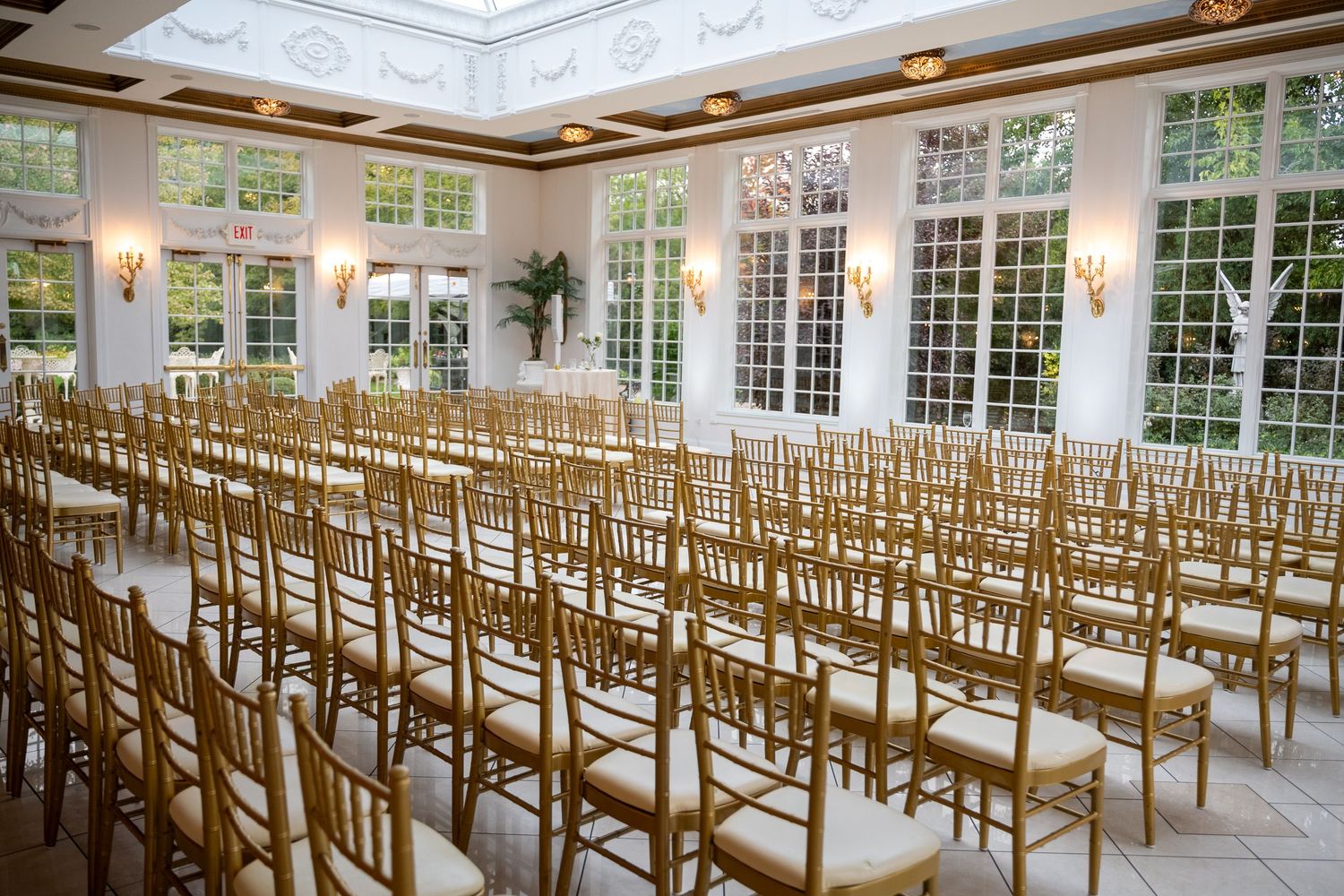 Elegant white wedding ceremony space with rows of wooden chairs and large windows letting in natural light.