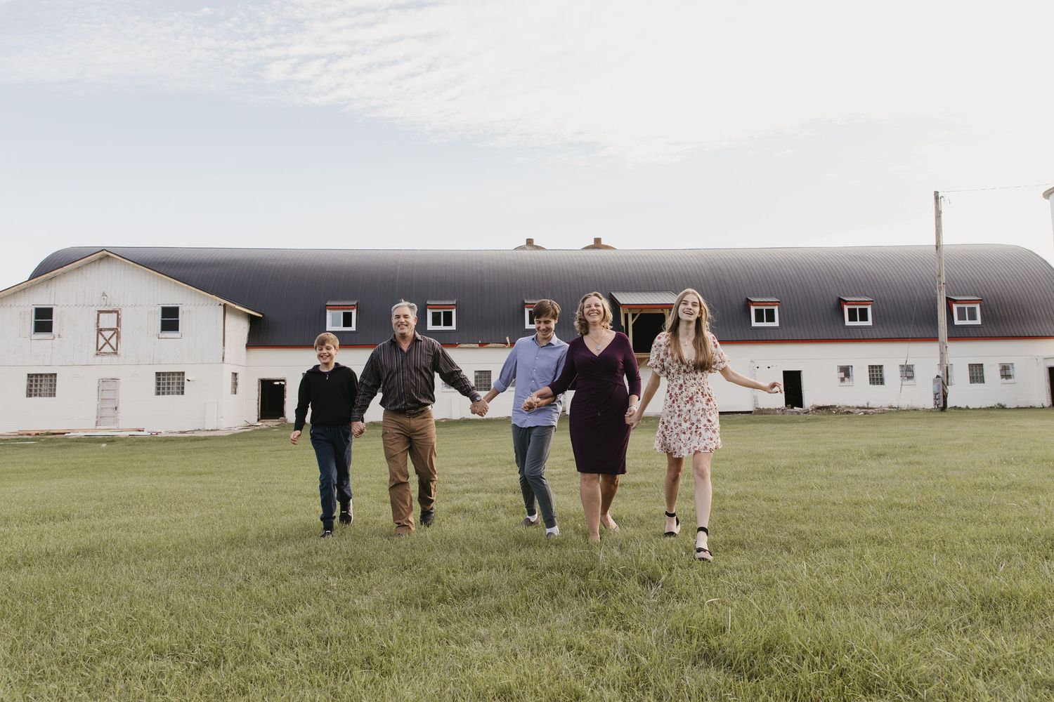 Group of people walking across a grassy field with white buildings in the background on an overcast day.