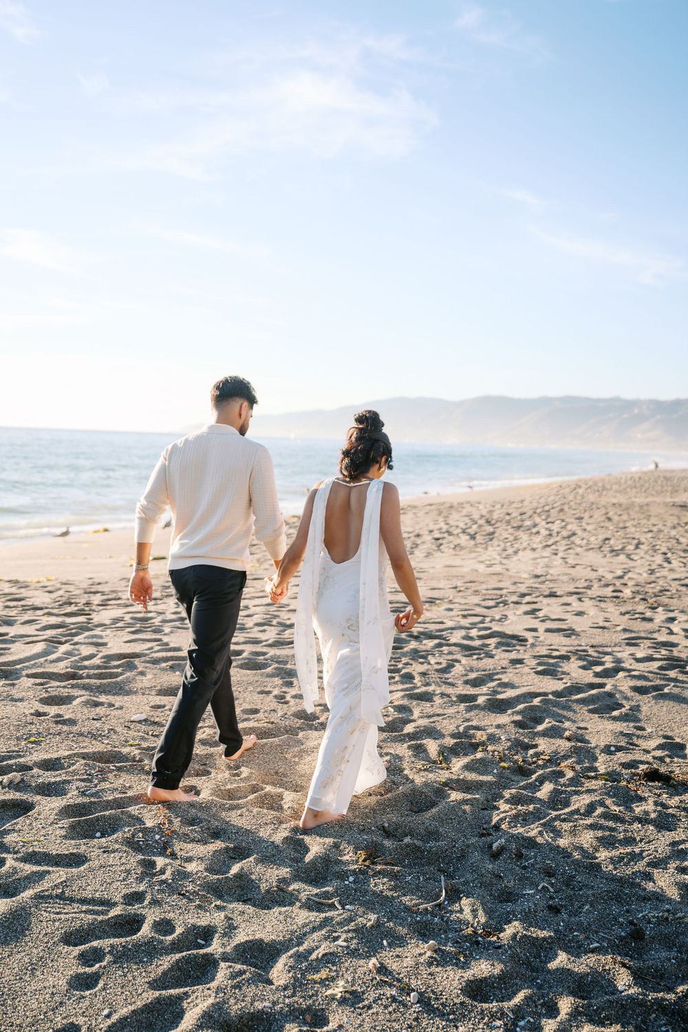 A couple walking together on a sandy beach holding hands during a sunny day at the ocean shore.