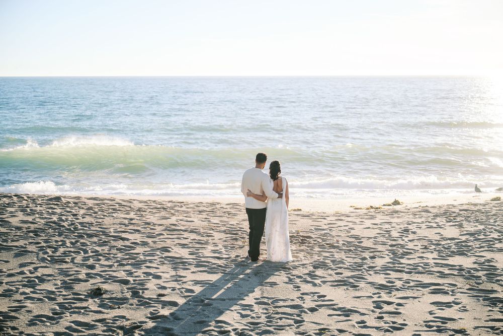 A couple shares a romantic moment on a sandy beach during sunset with waves crashing in the background.