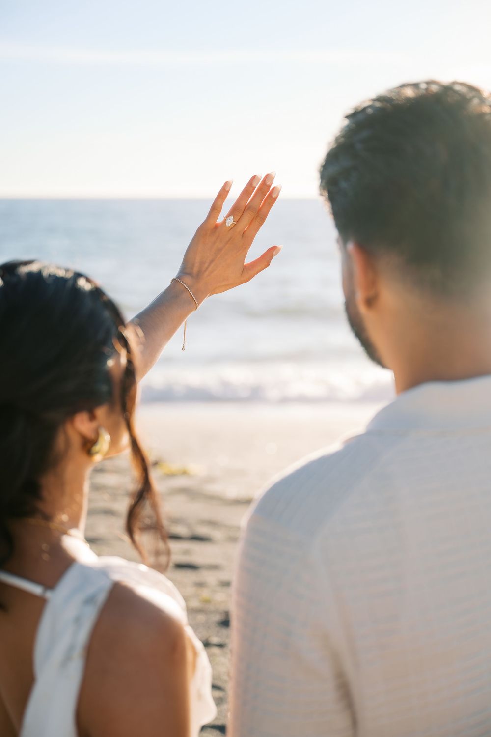 A group of people raise their hands in unison while standing on a sunny beach at sunset.