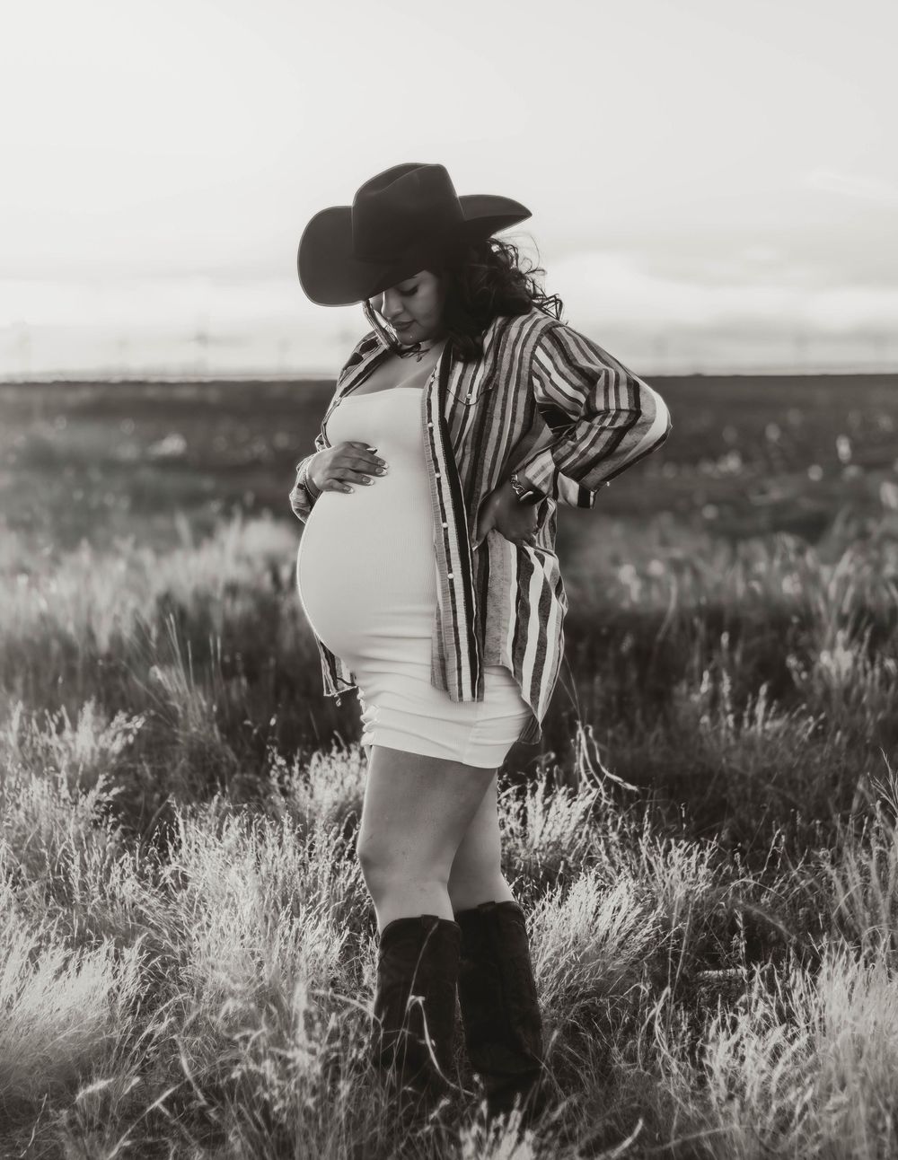Black and white maternity portrait with cowboy hat in tall grass.