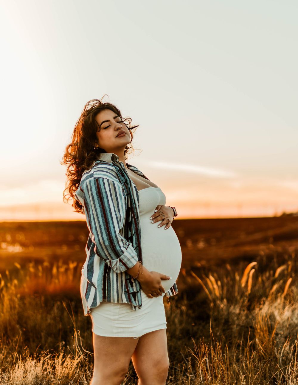 Maternity photo in striped shirt against sunset prairie landscape.