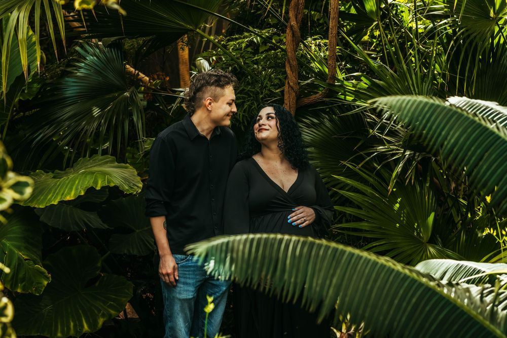 Couple in black outfits sharing a romantic moment surrounded by lush tropical greenery.