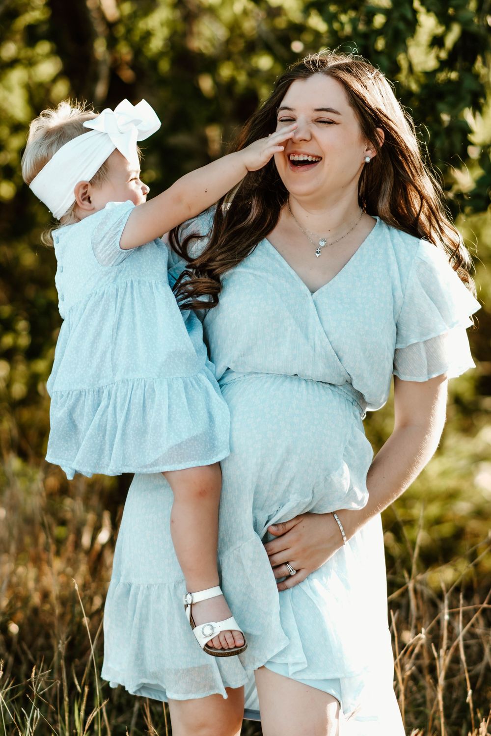 Joyful outdoor photoshoot featuring matching light blue dresses in a sunny garden setting.