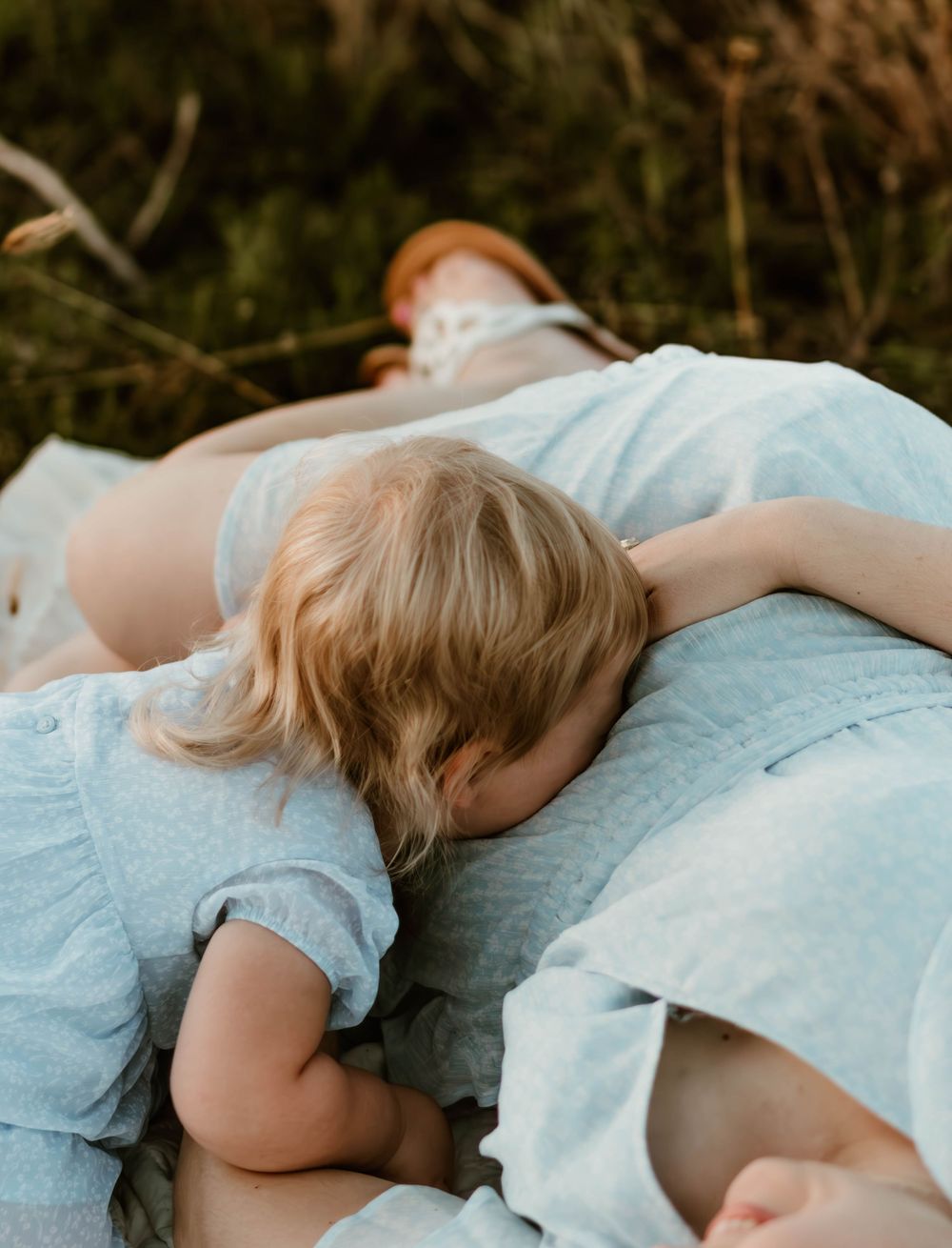 Intimate maternity photo showing tender moment between family members in matching blue dresses.