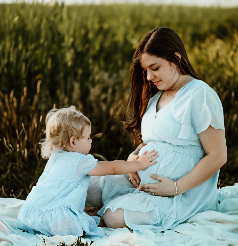 Sweet outdoor maternity session with matching blue dresses on a white blanket.