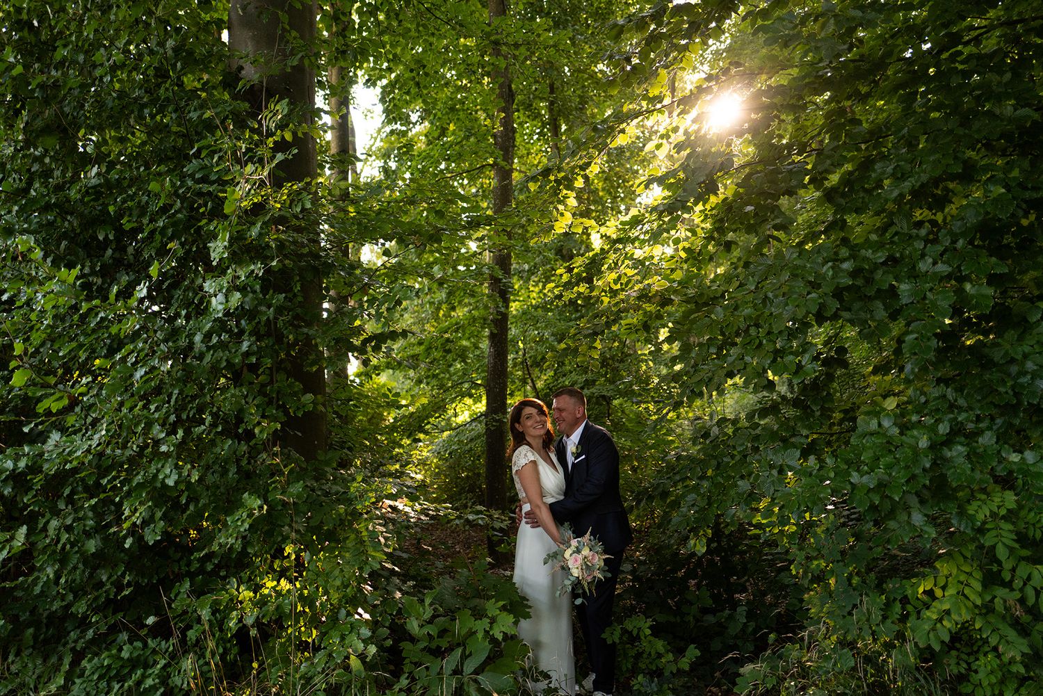 Natürliches Brautpaar-Shooting im dichten Schwarzwald, Sonnenstrahlen fallen durch die Bäume, ehrliche und ungestellte Hochzeitsfotografie.