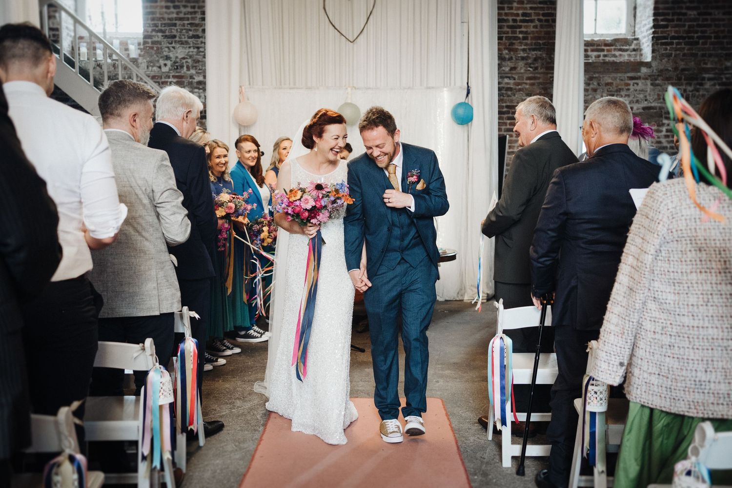 A couple shares a romantic moment together in front of an industrial building with a tall brick chimney.