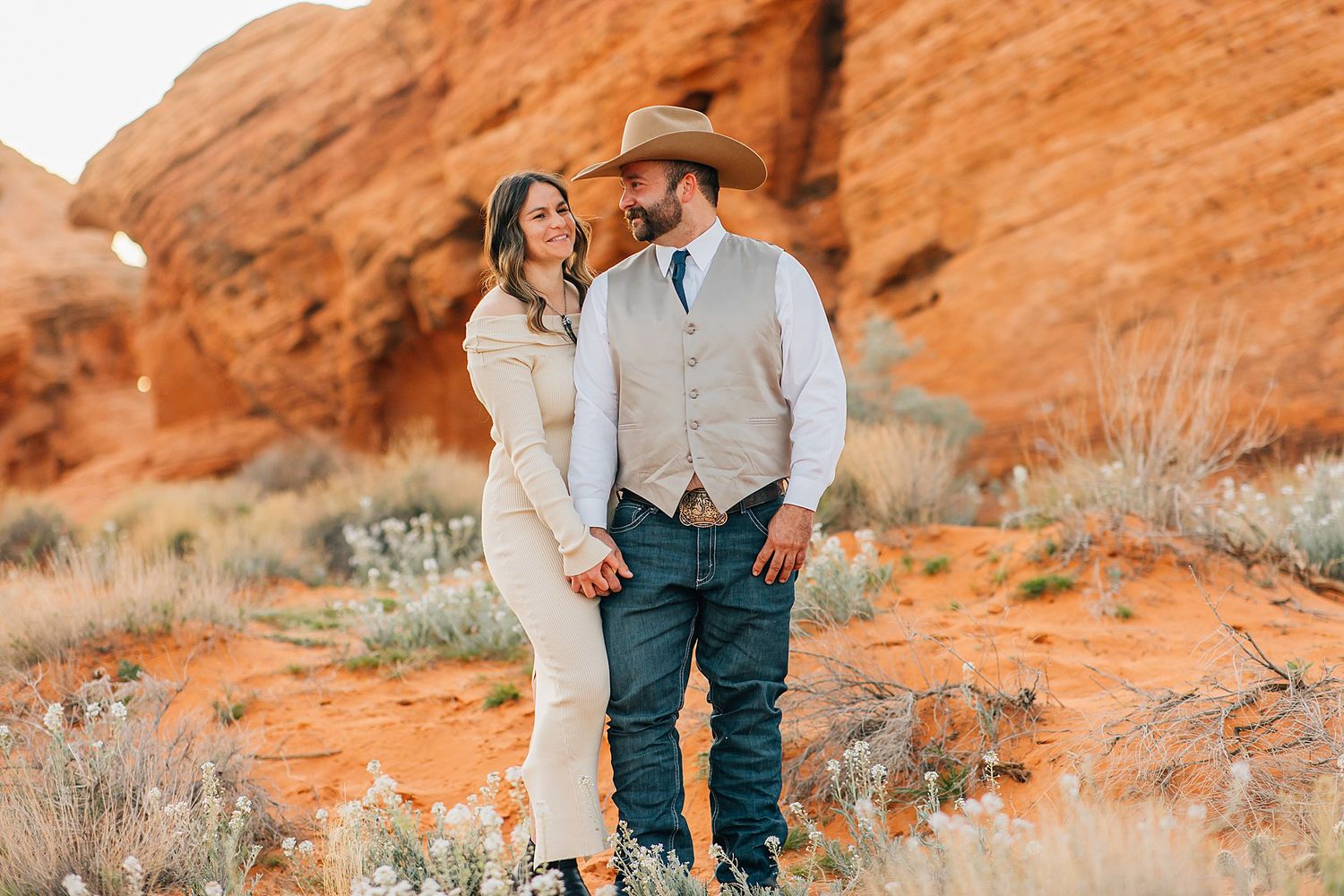 A couple embraces in a romantic moment against stunning red rock formations in the desert landscape.