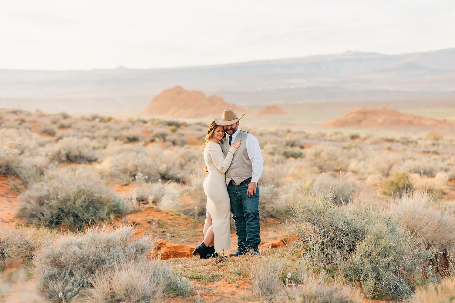 Desert engagement photoshoot with sage brush and red sandstone cliffs in the background.