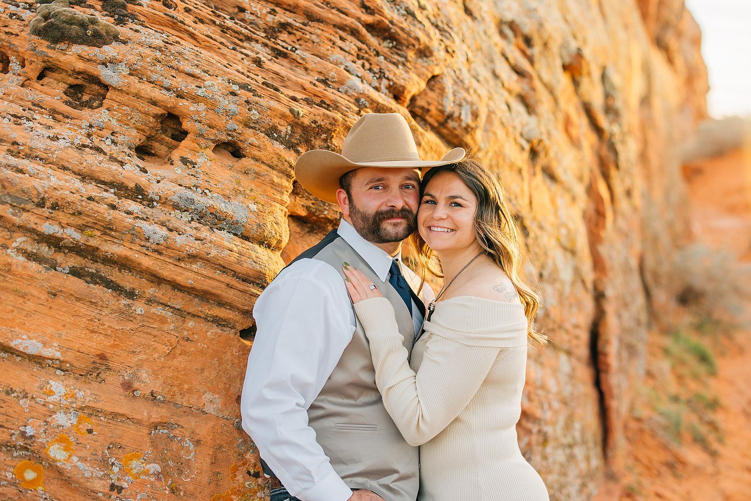 Romantic couple embracing near majestic orange sandstone cliffs during golden hour.