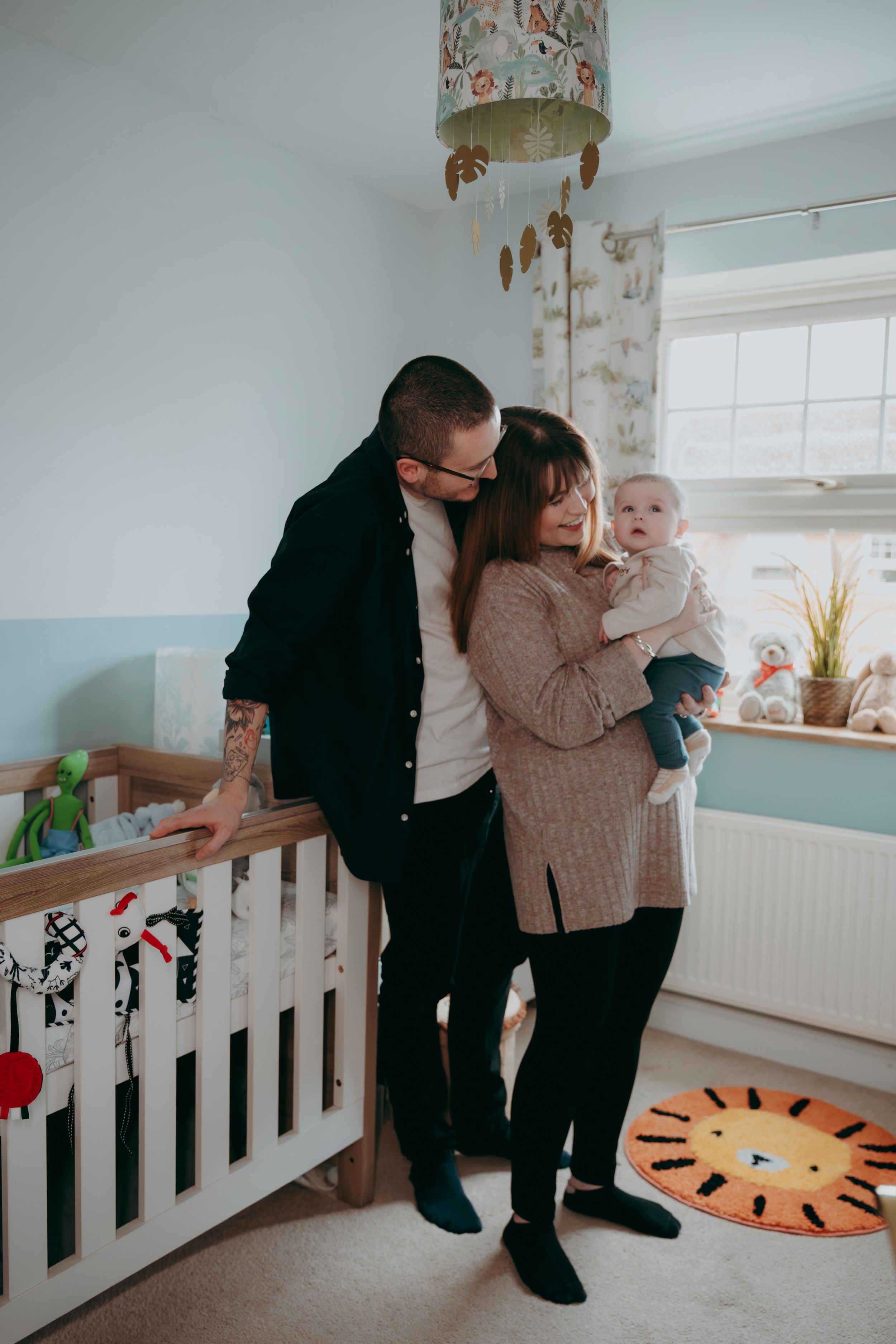 A cozy nursery scene with a decorative sun rug, white crib, and family sharing a tender moment together.